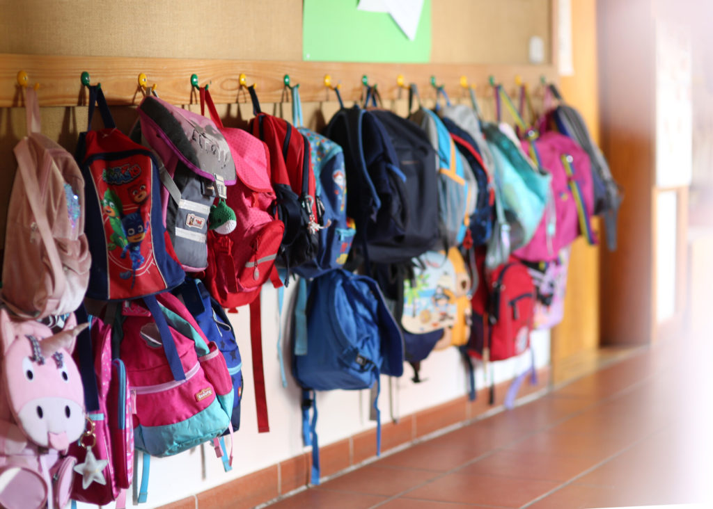 mehrere farbige Kleiderhaken in einer Kita, welche mit Kinderrucksäcken behangen sind.