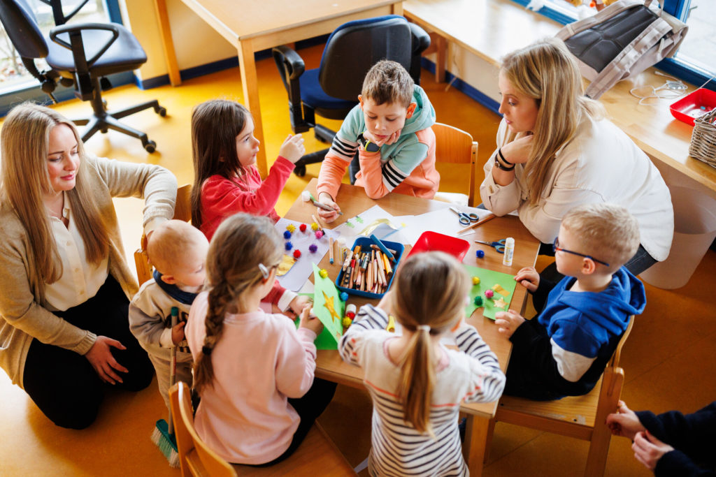 Kinder und Erwachsene sitzen am Tisch und spielen und malen gemeinsam.