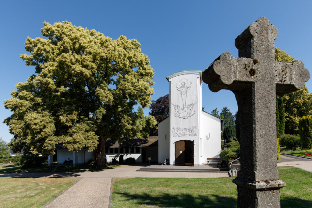 Steinkreuz und im Hintergrund eine Friedhofskapelle