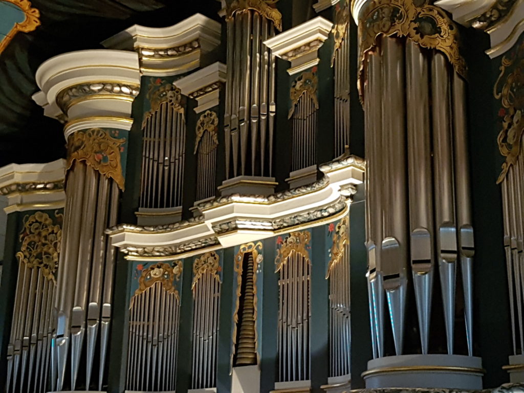 Orgelpfeifen mit hellblauer Holz-Vertäfelung. Goldene Verzierungen und Blumen auf der Vertäfelung.